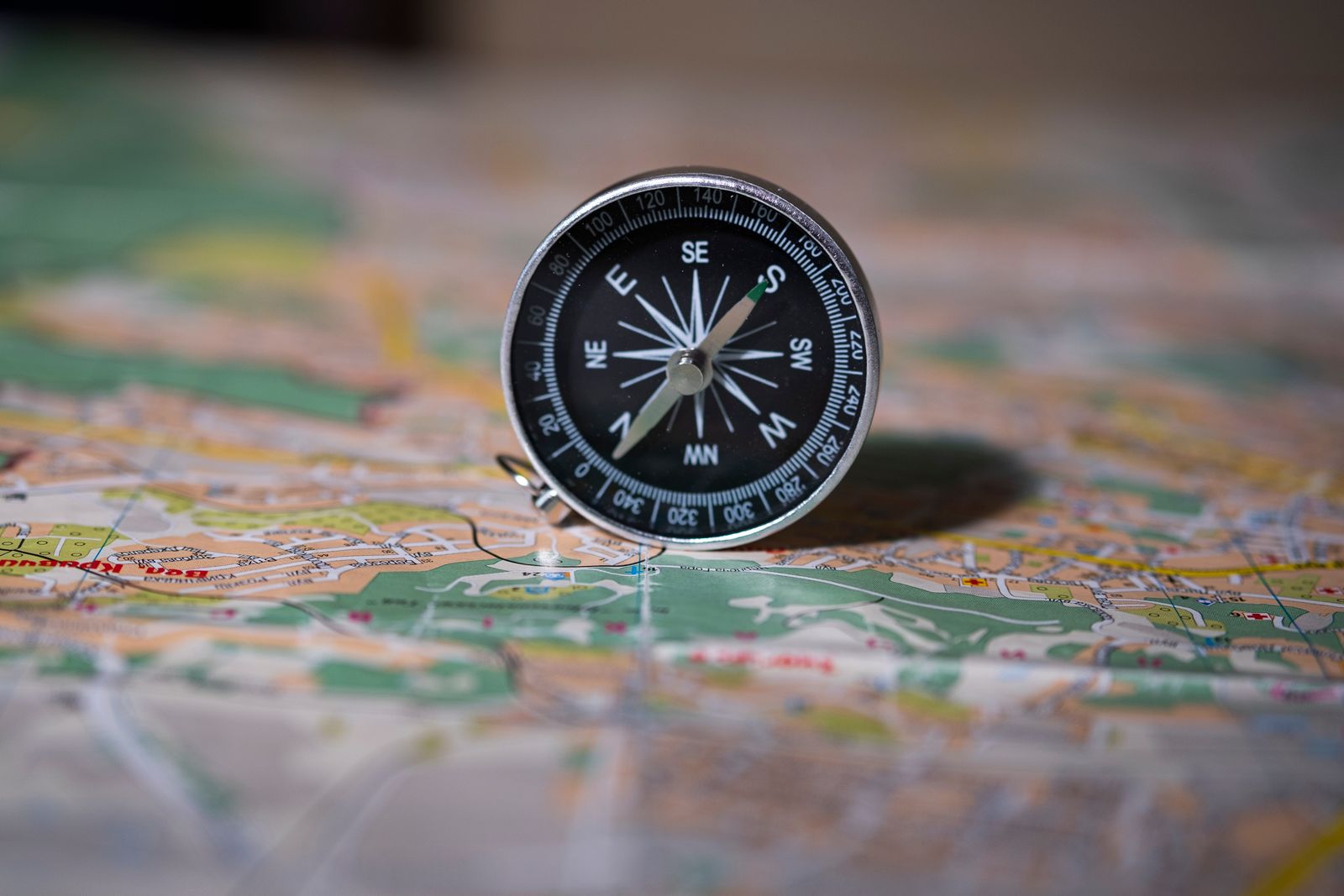 Bússola de metal apoiada em pé sobre um mapa aberto, com a agulha nítida em primeiro plano e o mapa se desfocando ao fundo, representando o instrumento que mostra a direção sem escolher o caminho pela pessoa