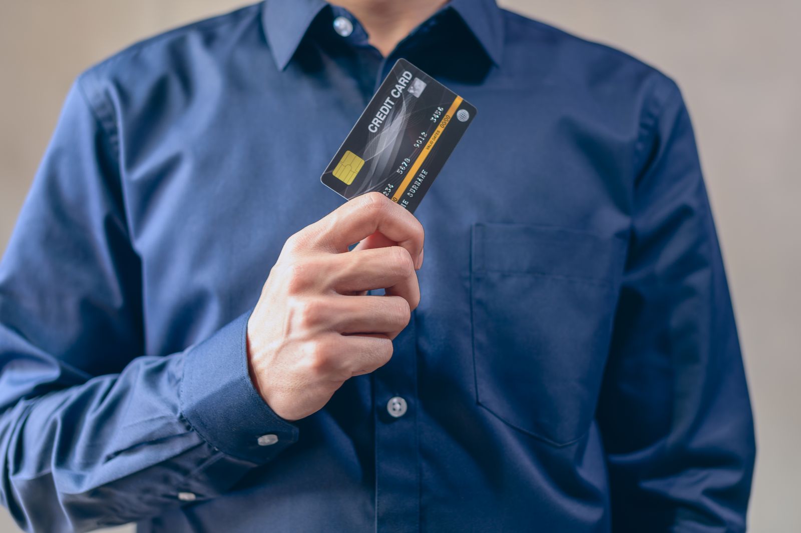 Homem de camisa azul-marinho segurando um cartão de crédito, o crédito caro que pesa no orçamento do cliente endividado