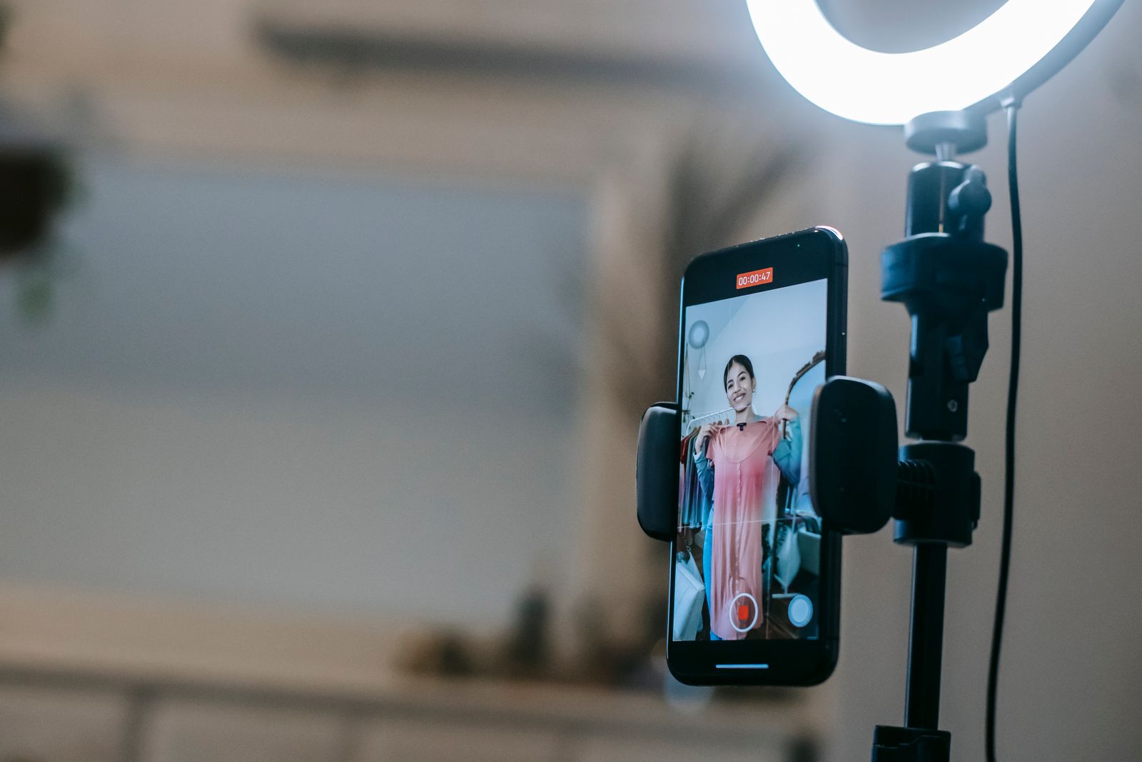 Celular montado em um tripé com iluminação de anel, gravando um vídeo com o tempo de gravação na tela, representando a rotina de quem produz conteúdo com o próprio telefone