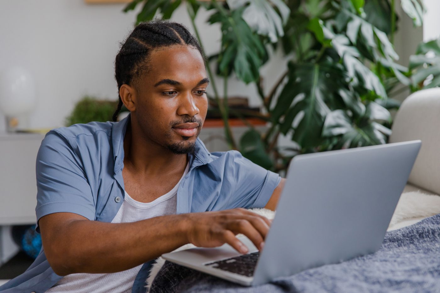 Homem de camisa azul concentrado, atendendo no notebook em casa, representando quem ganha uma renda extra com educação financeira nas horas vagas