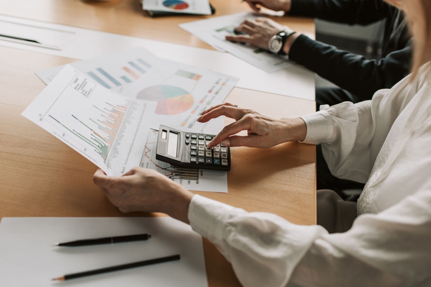 Duas pessoas analisando gráficos financeiros e usando uma calculadora sobre a mesa, montando o fluxo de caixa do cliente
