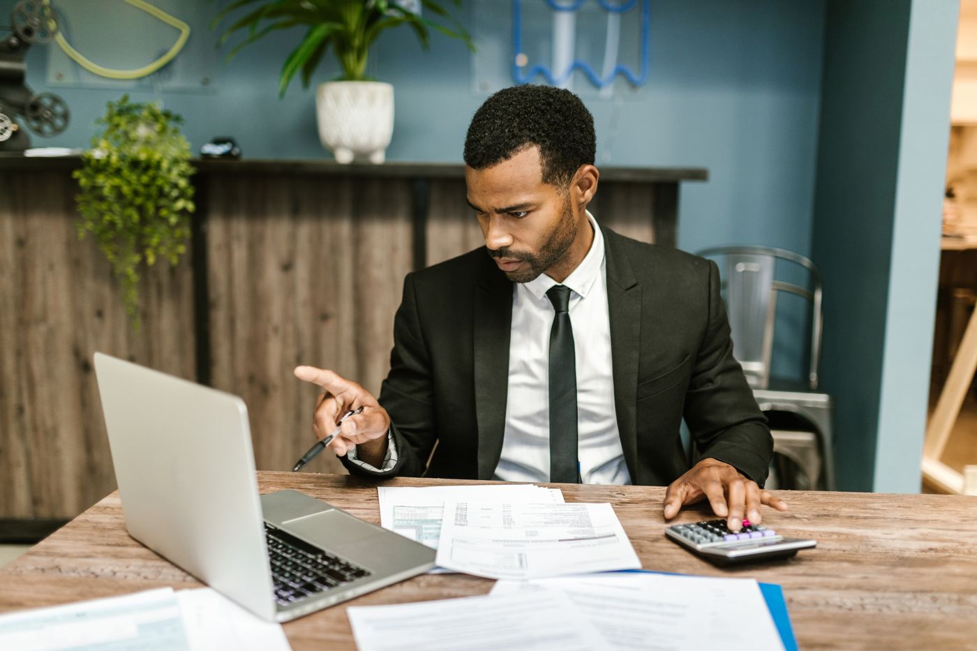 Educador Financeiro concentrado na mesa de trabalho, com laptop, relatórios e calculadora, no dia a dia do atendimento