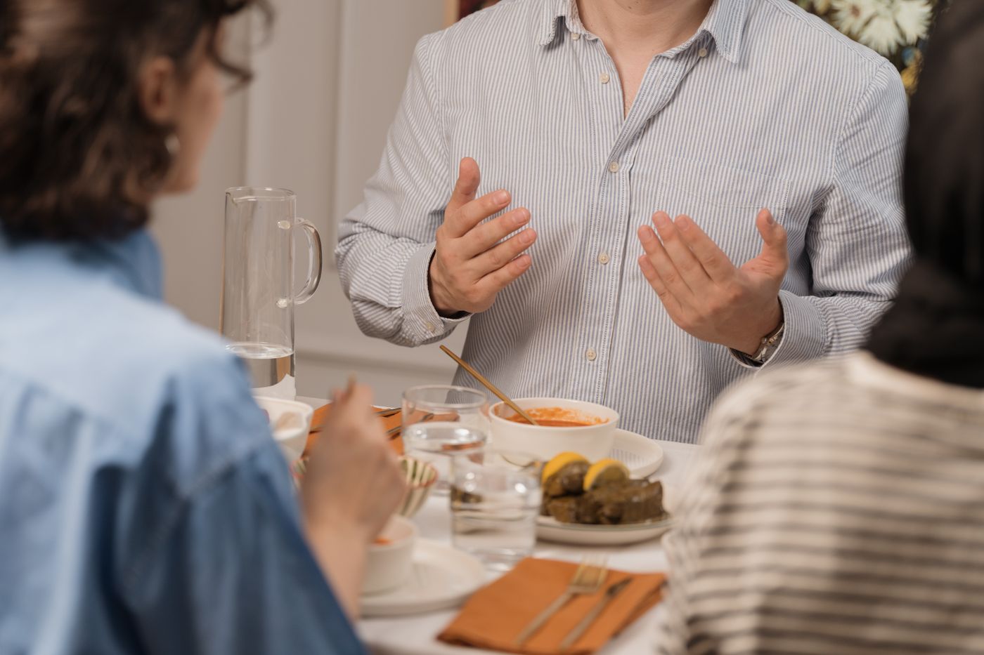 Pessoas sentadas à mesa de um almoço, uma delas gesticulando enquanto fala com as outras, representando a conversa em que o nome de um profissional de confiança é passado adiante