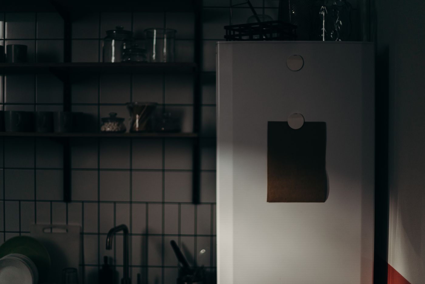 Cozinha à meia-luz com uma folha de papel presa por ímã na porta da geladeira, representando o plano que fica preso na geladeira e não vira rotina