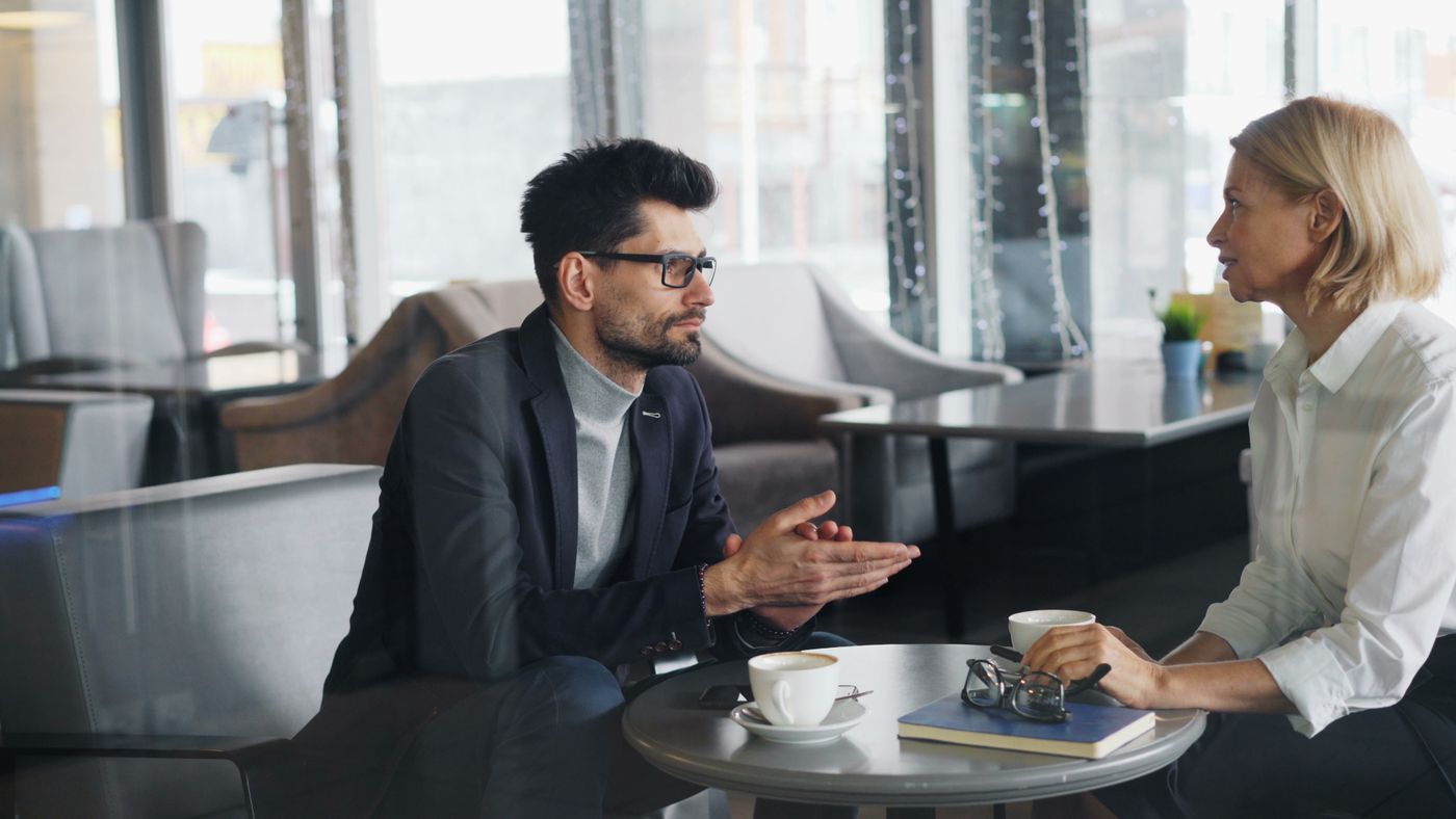 Dois profissionais conversando de forma próxima em torno de uma mesa com café, representando o primeiro passo de sentar com alguém de confiança para fazer o diagnóstico financeiro