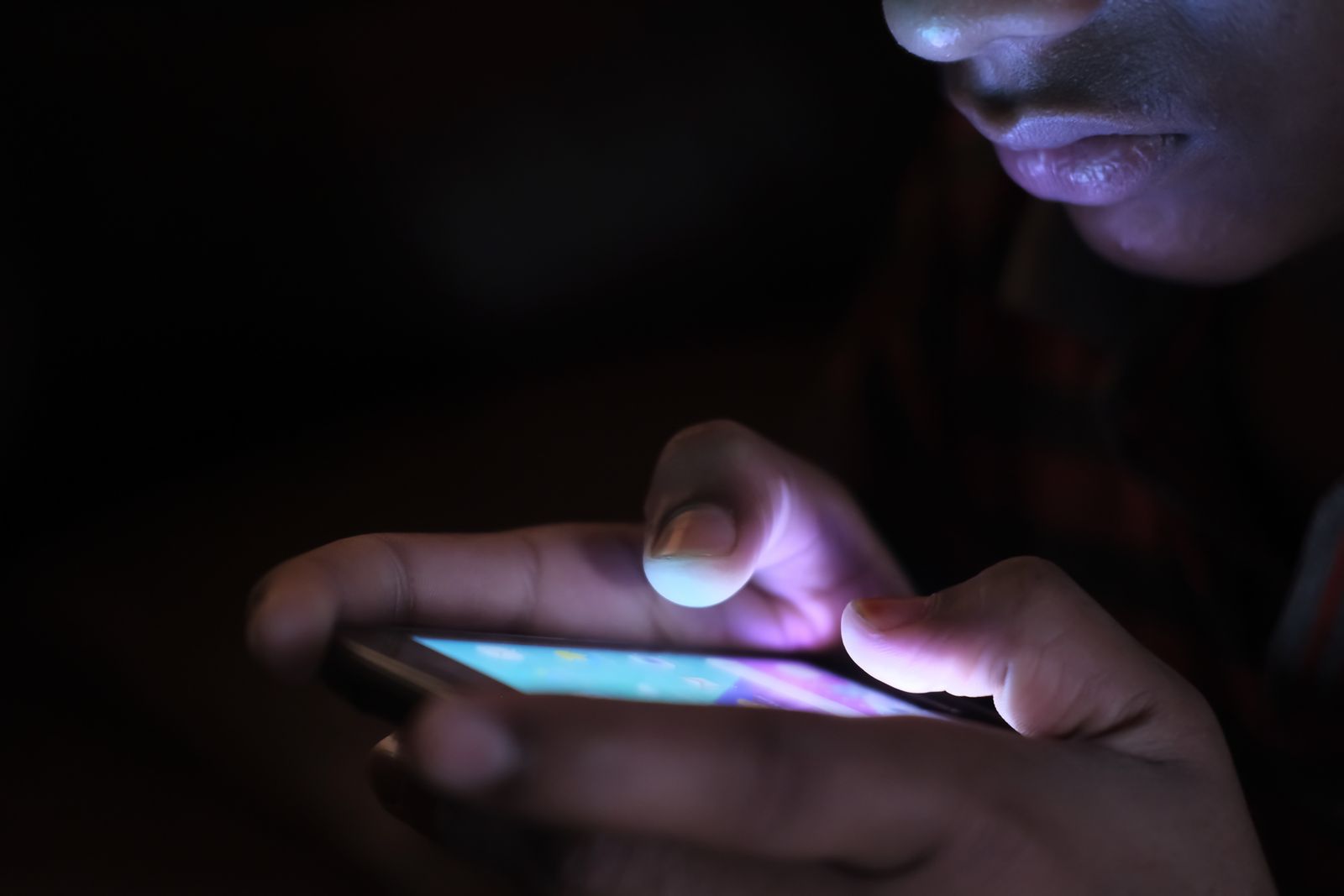 Close das mãos de uma pessoa digitando uma mensagem no celular no escuro, com o rosto iluminado pela luz azulada da tela, representando a conversa conduzida no direct